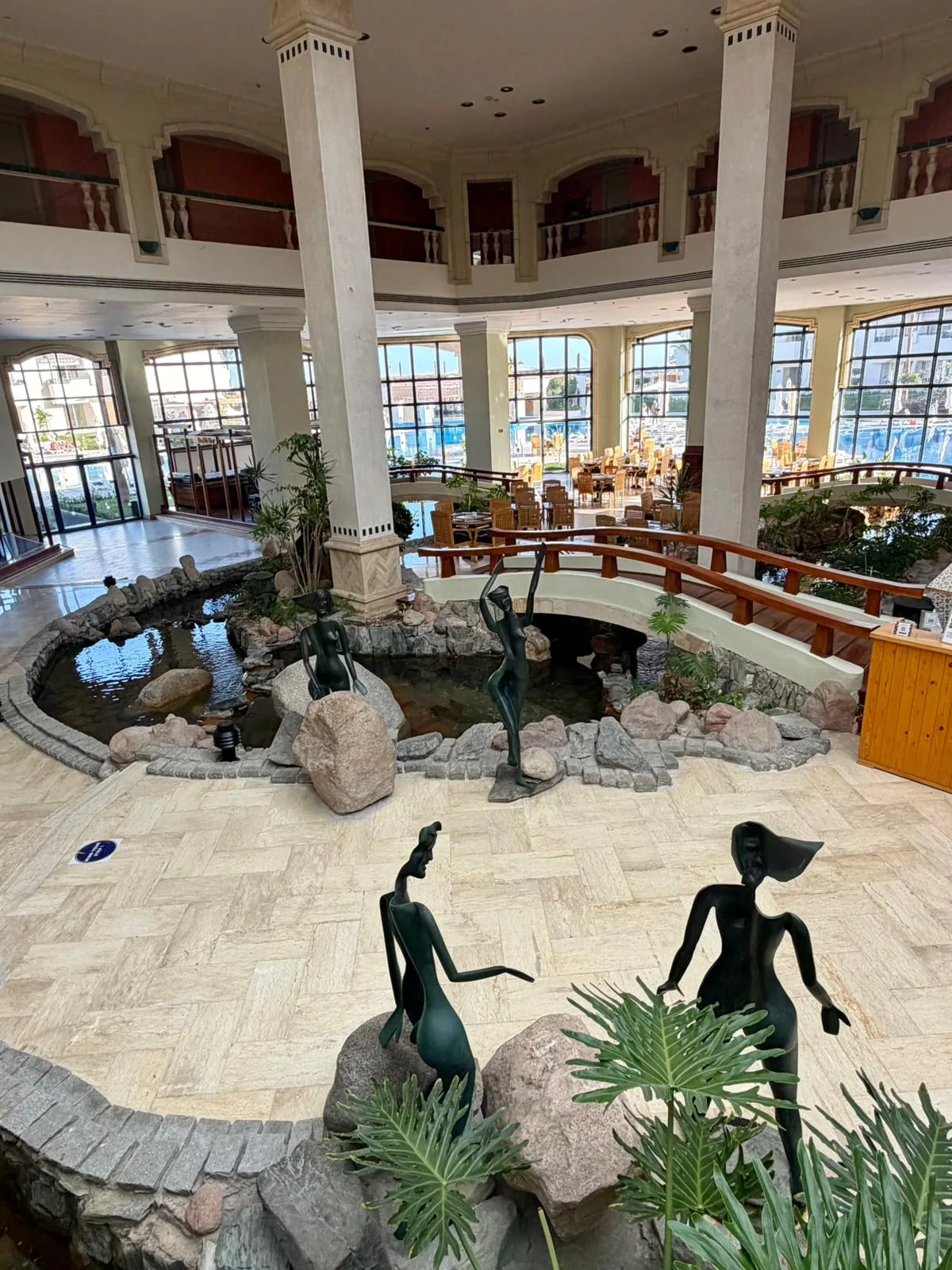 Hall central du Naama Bay Promenade Resort avec coupole, colonnes blanches et bassin abritant trois sculptures de bronze figurant des silhouettes féminines stylisées